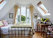 Yellow quilt on double bed with open doors and view to Oxfordshire countryside, UK