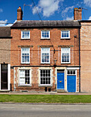 Dreistöckiges Backsteinhaus mit hellblauer Eingangstür in Deddington, Oxfordshire, UK