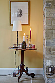 Lit candles on side table with gilt framed artwork in Northumberland farmhouse, UK