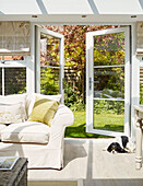 Weißes Sofa mit offenen Gartentüren zum Garten in einem Wintergarten in North Yorkshire, UK