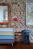 Decorative stove with upcycled chest of drawers and mirror against exposed stone wall in Brittany cottage, France