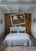 Doppelbett mit freiliegender Steinwand, leerem Bilderrahmen und Lampen in einem bretonischen Landhaus in Frankreich