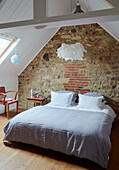 Doppelbett in einem aus Naturstein errichteten Dachgeschoss eines bretonischen Landhauses in Frankreich
