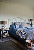 Lampenpaar am Bett mit blauer Bettdecke und Decken in einem Haus in Devon, UK