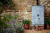 Metal water butt in garden of Cotswolds stone cottage, UK