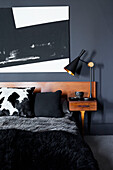 Moderne Kunst über dem Bett mit schwarzem Fellüberwurf und Nachttisch aus Holz in einem Haus in Ramsgate, Kent, UK