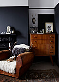 Vintage chest of drawers and worn leather armchair at fireside in Ramsgate home Kent, UK