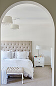 View through arch into bedroom with buttoned headboard in York home, UK