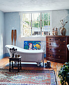 Slipper bath and vintage chest of drawers at window in Devon home, UK