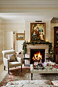 Armchair and ottoman set with wine and mince pies at fireside in Cotswolds home, UK