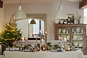 Pendant lights above dining table with lit candles and Christmas tree in West Sussex home, UK