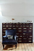 Dark blue velvet armchair and dark wood apothecary drawers in West Sussex home, UK