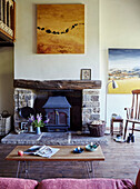 Modern art above exposed stone fireplace in double height Yorkshire farmhouse renovation, UK