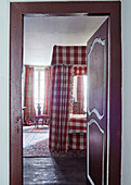 View through painted doorway to gingham four poster bed in Foix townhouse Ariege, France