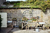 Pflanzen wachsen auf dem Wellblechdach über einer römischen Uhr und einem Tisch im Hof eines Bauernhauses in North Yorkshire, UK
