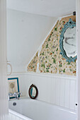 Light blue decorative mirror with floral wallpaper above recessed bath in Oxfordshire farmhouse, UK