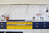 Bright yellow range with blue units and marble splashback in North Yorkshire farmhouse kitchen, UK