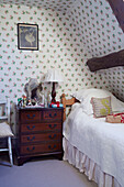 Single bed with wooden chest of drawers and floral wallpaper in, UK cottage