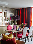 PInk dining chairs at table with curtains in hues of red London apartment, UK