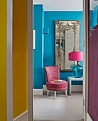 Decorative mirror and chair with table lamp viewed through bedroom doorway in London apartment, UK