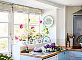 Cut flowers and sunhat on draining board at window with pink geraniums in, UK cottage
