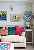Framed artwork above sofa with velvet cushions and lamp in, UK cottage