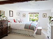 Doppelbett mit grauer Decke und gerahmten botanischen Drucken in einem weiß getünchten Cottage-Schlafzimmer, UK