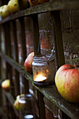 Stilleben mit Äpfeln und Kerzen in Gläsern an einem Spalier vor einer Backsteinmauer