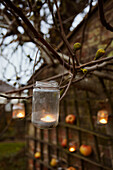 Tealights in jam jars hanging from trees light a night garden