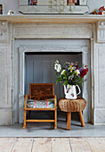 Cut flowers on stool with child's rocking chair in recessed marble fireplace of Colchester family home, Essex, England, UK