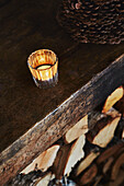 Tea light burning in glass holder on mantlepiece above logs in Wooden cabin situated in the mountains of Sirdal, Norway