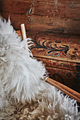 Detail of fluffy sheepskin on an armchair beside a painted chest inside a Wooden cabin situated in the mountains of Sirdal, Norway