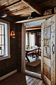 Blick aus der holzverkleideten Diele durch offene Tür ins Kinderzimmer mit Tisch, in einer Holzhütte in den Bergen von Sirdal, Norwegen