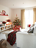 Tartan blanket on ottoman with white sofa in Polish family home at Christmas