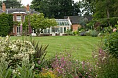 View on cottage and conservatory from backyard, with flourishing flowers on foreground