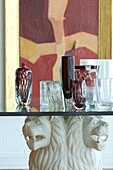 Still life with glass vases on table with carving lion heads painting in the background