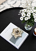 Schnittblumen und Buch mit silbernem Kerzenhalter auf schwarzem Couchtisch in einem Haus in Reigate, Surrey, UK