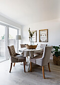 Blattarrangement auf rundem Esstisch mit Stühlen vor Terrassentüren in einem Haus in Reigate, Surrey, UK