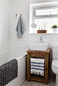 Striped towels in bathroom with wooden washstand below window in Reigate home, Surrey, UK