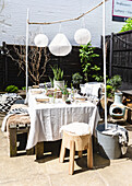 Solar lanterns above table with rustic seating and cushion fabrics in Colchester terrace, Essex, UK