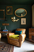 Eine Sammlung vergoldeter Vintage-Spiegel und Bilderrahmen hängt an der dunkelgrünen Wand, um die gemütliche Sitzecke interessant zu gestalten, in der ein Paar Vintage-Ledersessel bequeme Sitzgelegenheiten bieten