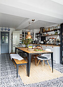 White scandinavian Style kitchen with patterned floor tiles and wooden table and bench seats with salad lunch, Cardiff, Wales, UK