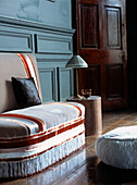 Upholstered small sofa with trimmings in large Georgian painted wood paneled room with wooden floor boards