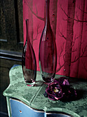 Detail von zwei violetten Glasflaschen und einer unechten violetten Blume auf einer überdachten Anrichte