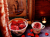 Detail von zwei Bechern mit in Wasser schwimmenden roten Rosen auf einem Kaminsims zur Dekoration