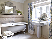 Freestanding rolltop bath with floral curtains in bathroom of Gloucestershire farmhouse, England, UK