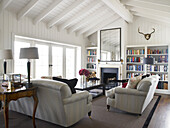 Bookcase and seating area in sunlit living room conversion of Hampshire farmhouse, England, UK