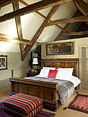 Carved antique bed with contemporary striped ottoman in beamed attic conversion of Georgian townhouse, Laughame, Wales, UK