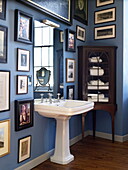 Pedestal basin with antique storage cabinet and artwork in blue bathroom of Georgian townhouse, Laughame, Wales, UK