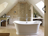 Freistehende Badewanne im gefliesten Dachgeschoss-Badezimmer eines Landhauses in Gloucestershire England UK